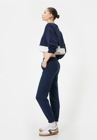 Marineblauwe cropped sweatshirt met een witte onderpanel, gecombineerd met marineblauwe joggers met elastische boorden en zakken, gedragen met witte sneakers.