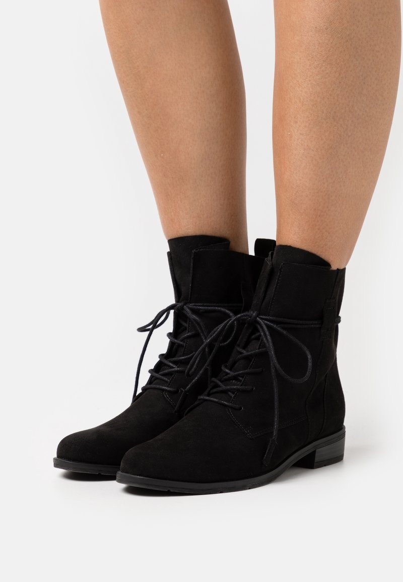 Bottines en daim noir avec un bout arrondi, un design à lacets et un petit talon bloc. Elles présentent des détails de couture et une texture douce.