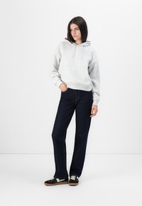 Felpa grigia con tasca a marsupio, abbinata a jeans dritti blu scuro. Sneakers nere con dettagli bianchi completano l'outfit.