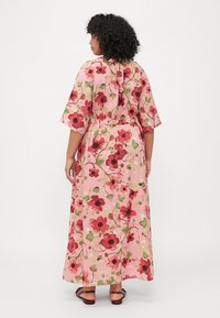 Maxi dress in pink with a floral pattern featuring red and green accents. Loose fit, short sleeves, and a gathered waist at the back.