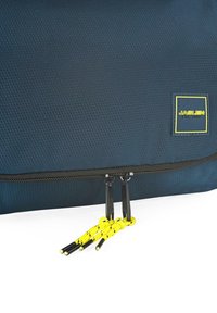 Bolsa de tejido texturizado en azul marino, con un zipper negro y tiradores de acentuación amarillos. Presenta una pequeña etiqueta de marca amarilla y negra.