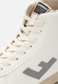 Sapatilhas altas em material sintético branco suave com detalhes em cinza claro. Apresentam atacadores texturizados, colarinho almofadado e detalhe do logotipo na lateral.