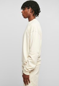 Helle beige Sweatshirt mit Rundhalsausschnitt, überschnittenen Schultern und gerippten Bündchen. Weicher Stoff, lässiger Schnitt und passend dazu Jogginghosen.