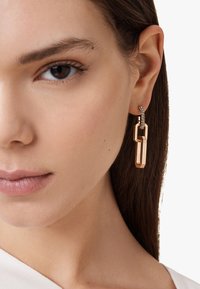 Orecchini pendenti color oro con un design a catena e dettagli di pietre trasparenti, che presentano una finitura lucida e una forma geometrica.