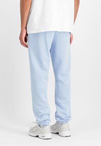 Világoskék, puha anyagból készült melegítőnadrág, elasztikus szegéllyel és hátsó zsebbel, fehér sneaker cipőkkel, semleges háttér előtt.