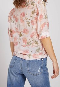Bloem blouse met zachte roze en groene patronen, lichtgewicht stof, korte pofmouwen en opgerolde manchetten, gedragen met lichtblauwe distressed jeans.