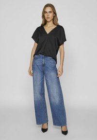 Top in satin nero con scollatura a V e maniche corte, abbinato a jeans in denim blu a vita alta e gamba larga. Tacchi a punta nera completano il look.