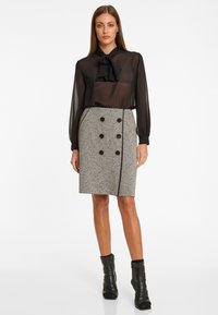 Zwarte doorschijnende blouse met strik en lange mouwen, gecombineerd met een grijze tweed kokerrok met dubbelgebreide knopen. Zwarte enkellaarsjes.