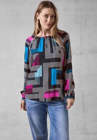 Svart blus med färgglada geometriska mönster i blått och magenta, med rund halsringning och långa ärmar, tillverkad av lättviktsmaterial.