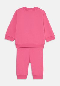 Ensemble de jogging en coton rose comprenant un haut à manches longues avec un col rond et un pantalon fuselé assorti, tous deux avec des poignets côtelés.