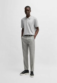 Polo gris de manga corta con un patrón sutil, combinado con pantalones de sastre gris claro y zapatillas negras, con un cinturón negro elegante.