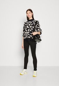 Black and white patterned sweater, textured with a fuzzy finish, paired with black leggings and white sneakers featuring yellow accents.