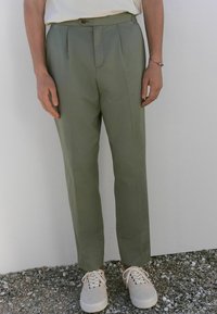 Pantalons ajustés vert clair avec une coupe droite, des plis à l'avant et une fermeture à bouton, associés à des baskets blanches.
