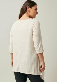 Tunica beige chiaro con maniche a tre quarti, realizzata in un tessuto a maglia testurizzato con sottili motivi a pois e un design con orlo a forma di hi-low.