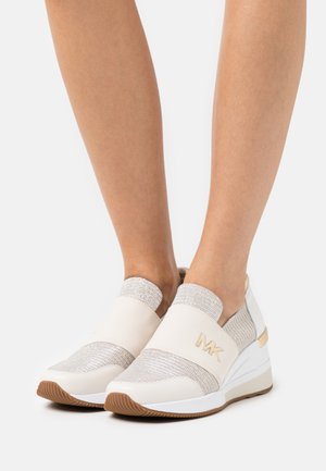 Sneakers bianchi slip-on con accenti metallici, bande elastiche, tomaia testurizzata e suola a zeppa. Presentano un logo impresso sul lato.