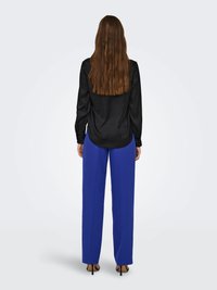 Schwarzes Satin-Hemd mit langen Ärmeln, kombiniert mit hoch taillierten, weiten royalblauen Hosen. Glatte Textur, einfarbige Farben und offenes Rückendesign.