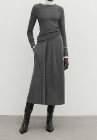 Grå ribbad långärmad topp i kombination med en högmidjad grå plisserad kjol. Svarta knähöga stövlar kompletterar hela outfiten.