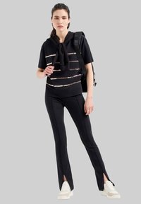 Zwart sportoutfit met een kortaf mouwtop met metallic strepen en taperende broek met zijslitsen, gedragen met witte sneakers.