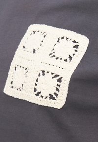 Quatre carrés floraux blancs en crochet disposés en grille sur un fond de tissu gris foncé.