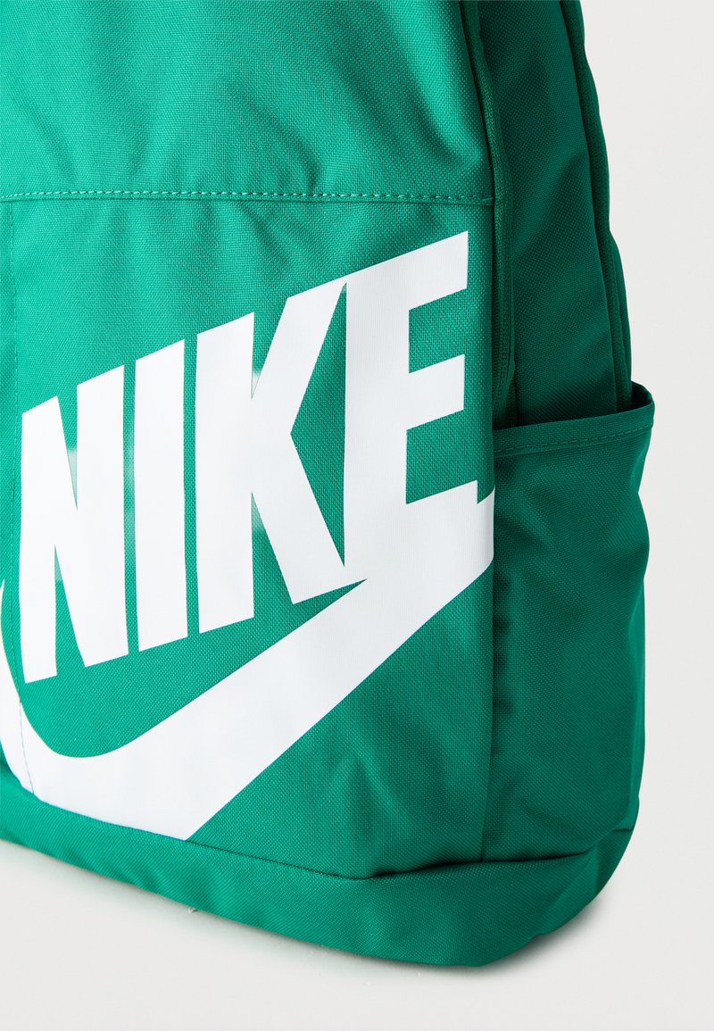 Grüner Stoffrucksack mit großem weißem Nike-Logo und Swoosh auf der Vordertasche, zeigt Seiten- und Bodendetails.