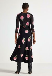 Abito nero a maniche lunghe con un motivo floreale di rose rosa, tessuto testurizzato e gonna fluida, abbinato a stivali neri con tacco al ginocchio.