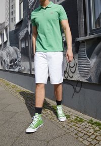 Grön polo-shirt med en liten logotyp, vita shorts och gröna högtoppsnikers. Outfiten har en avslappnad och bekväm design.