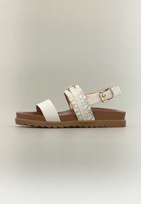 Λευκό και μπεζ φλατ σανδάλι με δύο μπροστινούς ιμάντες, λουράκι αστραγάλου με αγκράφα και καφέ σόλα με αυλακώσεις σε ουδέτερο φόντο.