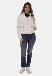 Giubbotto imbottito bianco con cappuccio, chiusura con zip e due tasche laterali; abbinato a jeans blu e sneakers bianche.