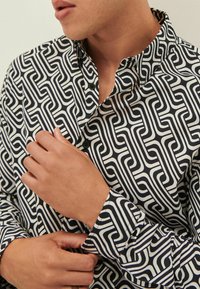 Camisa de patrón geométrico en blanco y negro con cuello, mangas largas, cierre de botones y textura de tela suave.