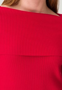 Haut rouge côtelé avec un col large et un design superposé. Présente des rayures verticales et une texture lisse dans l'ensemble.