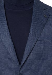 Granatowa marynarka w kratę z wywijanymi klapami, teksturowanym materiałem i pasującym golfem. Posiada małe logo na klapie.