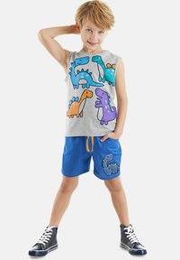 Gray sleeveless shirt with colorful dinosaur prints; blue shorts with orange drawstring and a dinosaur patch on the pocket; black high-top sneakers.