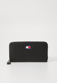 Cartera de cuero negro con un acabado texturizado, que presenta un parche de logo en azul, blanco y rojo en la parte frontal y un cierre tipo zip alrededor.