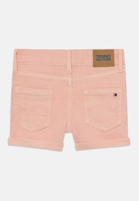 Jasnoróżowe dżinsowe szorty z podwiniętymi nogawkami, dwie tylne kieszenie z przeszyciami oraz brązowa metka z logo marki "TOMMY HILFIGER".