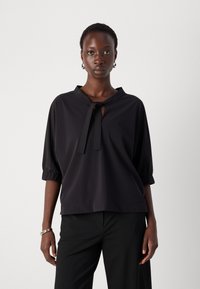 Zwarte korte mouwen top met een knoopnek, comfortabele pasvorm, subtiele gestreepte textuur en geplooide mouwen, gecombineerd met zwarte broek.
