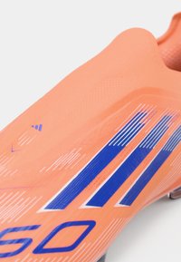 Oranssi jalkapallokenkä, jossa on teksturoitu päällinen sinisillä diagonaalisilla raidoilla ja logotiedolla, suunniteltu tiukkaan istuvuuteen. Kevyt rakenne.