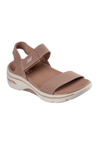 Sandalia de color rosa claro con correas de tela texturizada, cierres ajustables de Velcro y una suela blanca acolchada que presenta una ligera curva.