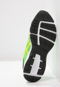 Zielony but sportowy z siatkową cholewką, czarną gumową podeszwą, białą wkładką, żółtymi akcentami oraz wzorzystym bieżnikiem dla lepszej przyczepności.