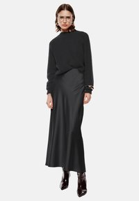 Maglione nero lavorato a maglia con collo alto, abbinato a una maxi gonna nera in satin elegante e stivali alla caviglia lucidi di un marrone scuro.