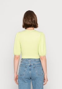 Top curto verde claro com mangas bufantes estruturadas e tecido texturizado. Combinado com jeans de ganga azul de cintura alta, mostrando a vista traseira.