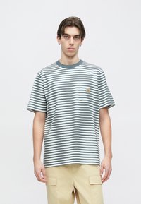 Ριγέ κοντομάνικο μπλουζάκι σε ανοιχτό γκρι και σκούρο μπλε, με στρογγυλή λαιμόκοψη και τσέπη στο στήθος με λογότυπο. Απαλό βαμβακερό ύφασμα.