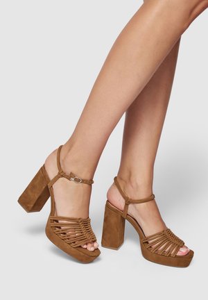 Braune Wildleder-Absatzsandalen mit einem klobigen Blockabsatz und geflochtenem Riemendesign. Knöchelriemen mit verstellbarem Schnallen-Detail, offene Zehen-Optik.