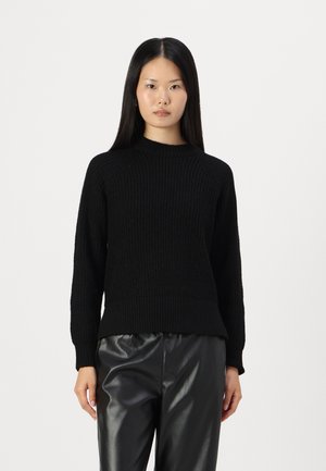 Pull en tricot noir avec une texture côtelée, col ras du cou et manches raglan, associé à un pantalon en cuir noir.