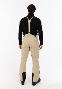 Beige skibroek met verstelbare banden, versterkte zwarte onderaccenten en een relaxte pasvorm. Soepele textuur voor comfort en bewegingsvrijheid.