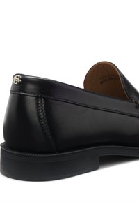 Μαύρο δερμάτινο μοκασίνι με λεία υφή, ραμμένες λεπτομέρειες και διακριτική ασημένια επιγραφή κοντά στη φτέρνα. Λαστιχένια σόλα για καλύτερη πρόσφυση.