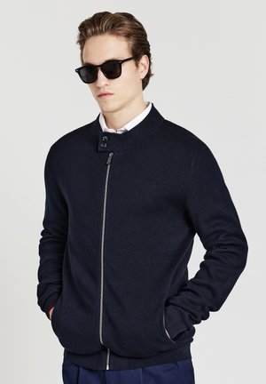 Sweat-shirt zippé marine foncé avec un col montant, un décolleté rond et des poignets côtelés. Matériau tricot léger, doté d'une fermeture à deux boutons.