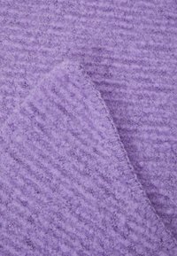 Tissu en laine violet doux avec une surface texturée et duveteuse et un détail de couture en diagonale visible.