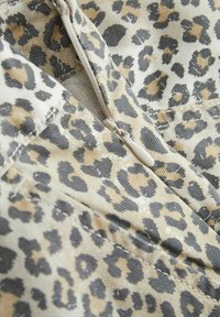 Tessuto animalier con macchie beige, nere e marroni. Presenta una chiusura con zip con un tirante beige e dettagli di cucitura visibili.