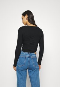 Black ribbed long-sleeve top paired with high-waisted blue denim jeans, featuring a relaxed fit and back pockets.