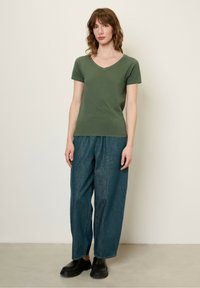 T-shirt verde oliva a V, maniche corte, silhouette aderente. Abbinato a pantaloni in denim scuri larghi e scarpe nere slip-on.